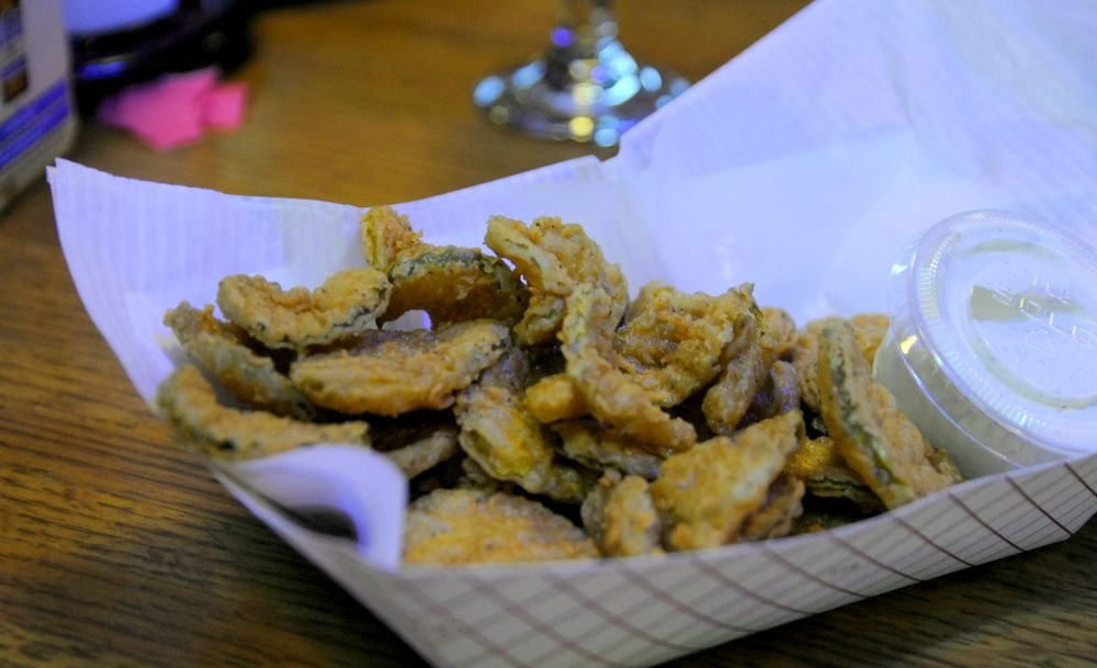 A paper boat of fried pickle chips with a cup of ranch