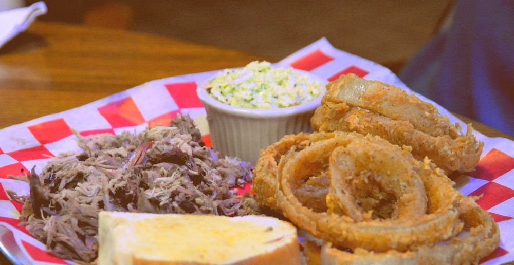Pulled pork plate with onion rings, coleslaw and grilled bread on checkered paper